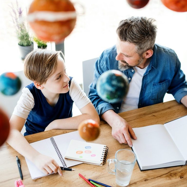 A man and a boy sit at a table, discussing a model solar system. Professional Tutors & Teachers. UK.