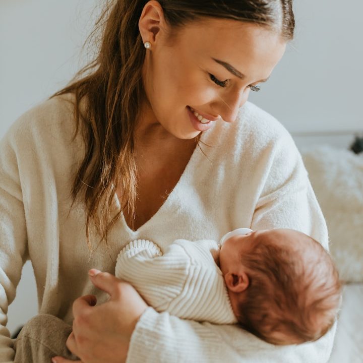 Smiling woman in a light sweater cradles a newborn baby in her arms. Nanny.