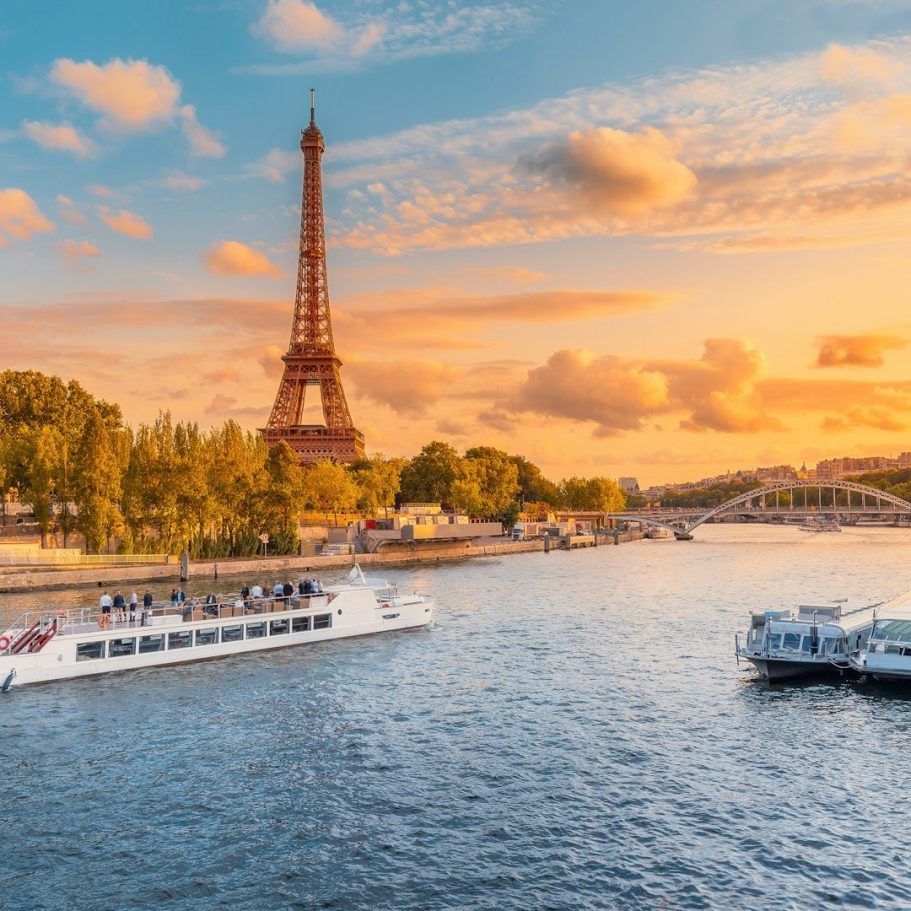 Sunset view of the Eiffel Tower beside the Seine River with boats and trees.