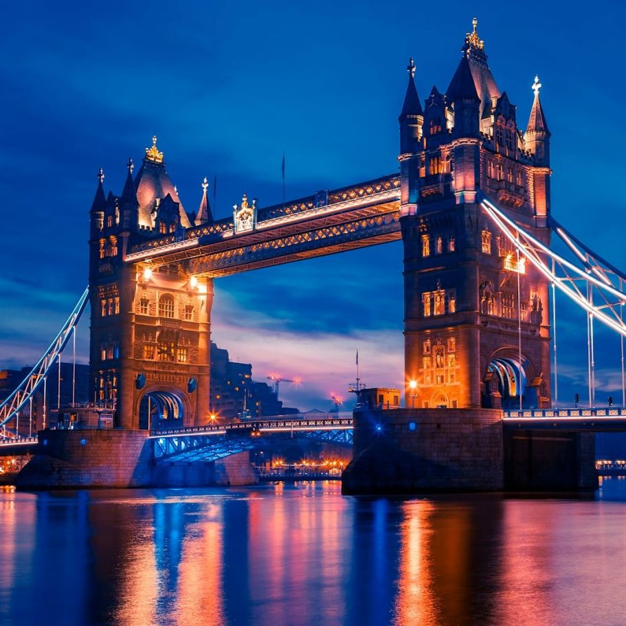 Tower Bridge illuminated at dusk, reflected in the River Thames.