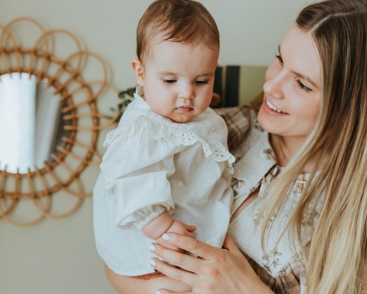 A mother holds her baby in a bright room, smiling at each other. Childcare and Education: UK Nanny Agency.